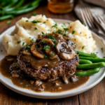 A rustic white dish filled with baked hamburger steaks in mushroom gravy, styled with mashed potatoes and a parsley garnish.