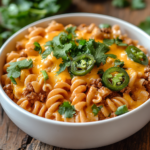Creamy One-Pot Taco Pasta topped with cheddar, jalapeños, and cilantro in a white bowl on a rustic table