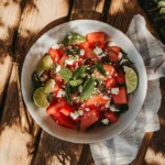 Fresh watermelon feta salad with mint served in a white bowl on a wooden table – summer side dish